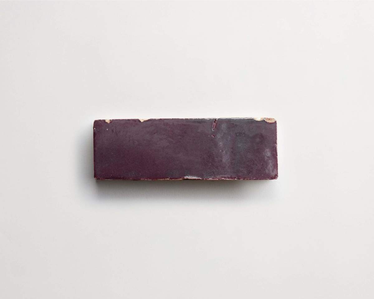 A rectangular, glossy, dark purple object, resembling a tile or a block, is positioned on a plain white surface.
