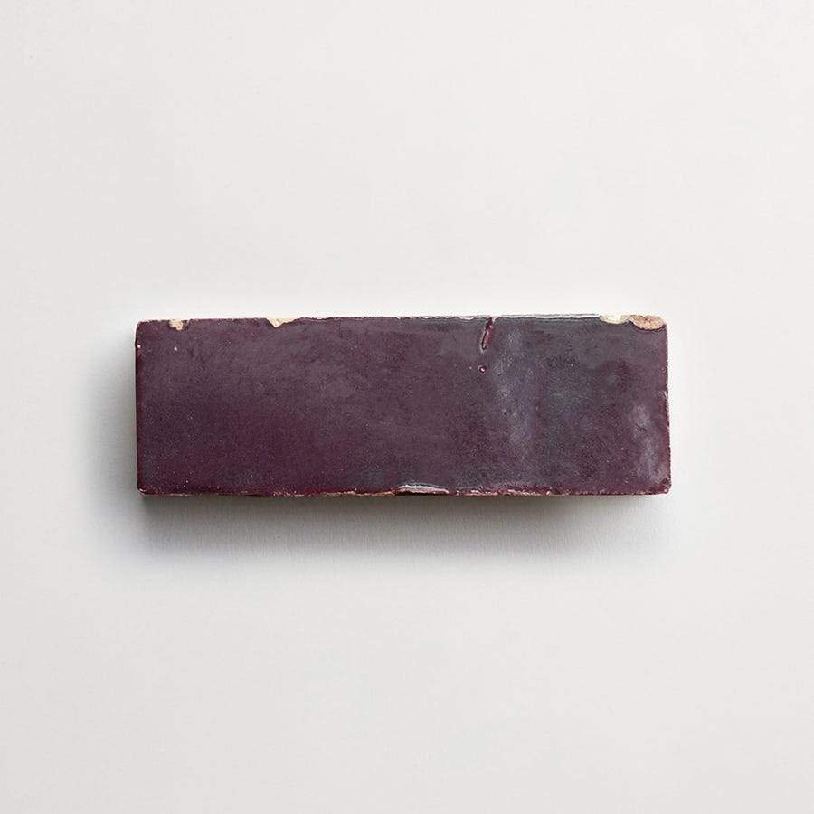 A rectangular, glossy, dark purple brick with slightly chipped corners on a plain white background.