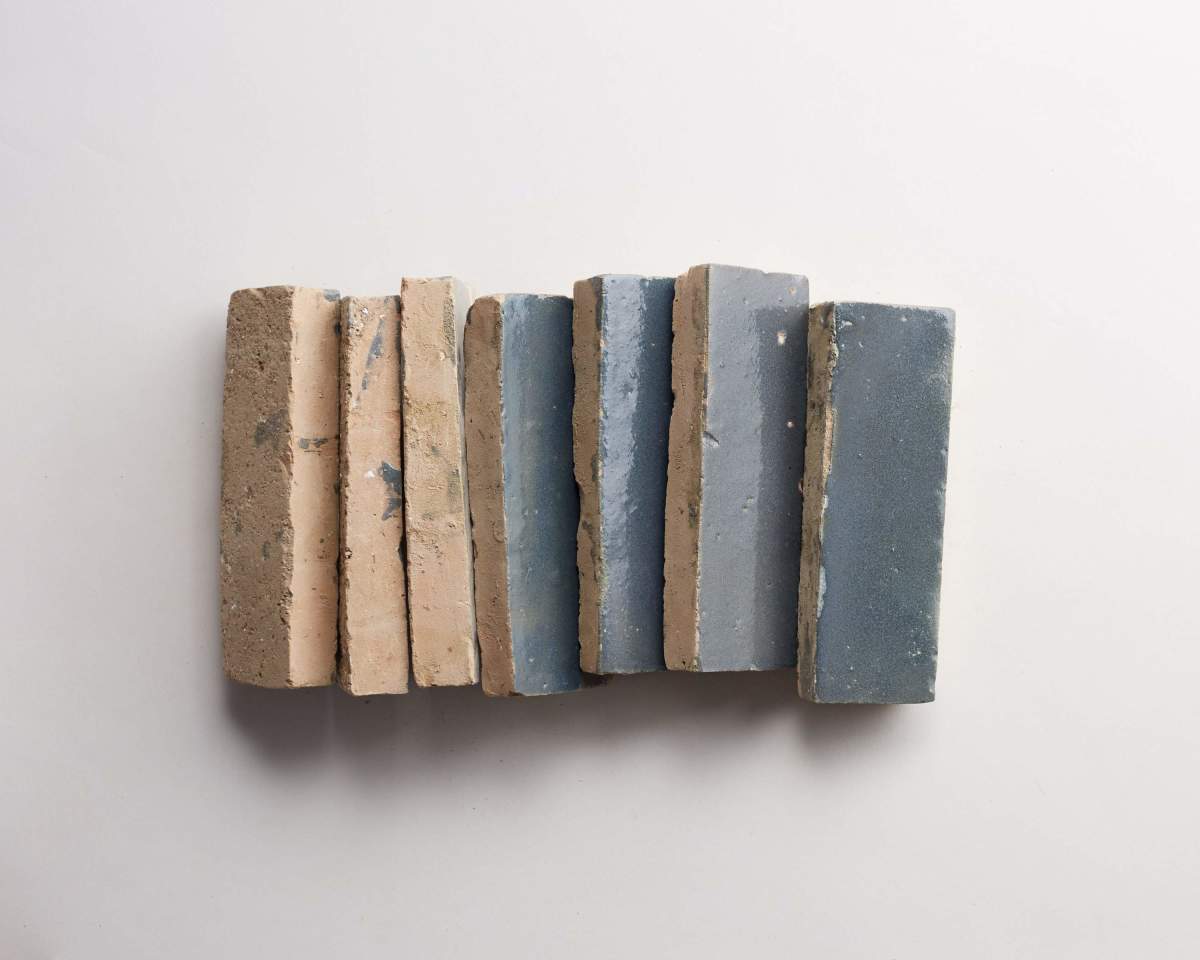 Seven rectangular clay bricks, arranged vertically on a white surface, with colors ranging from beige to various shades of blue.