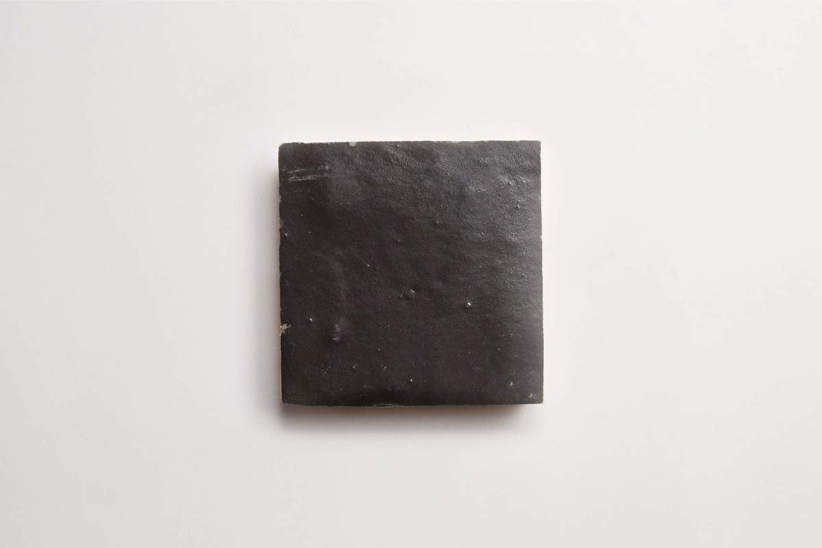 A single, square, black tile placed on a plain white background.
