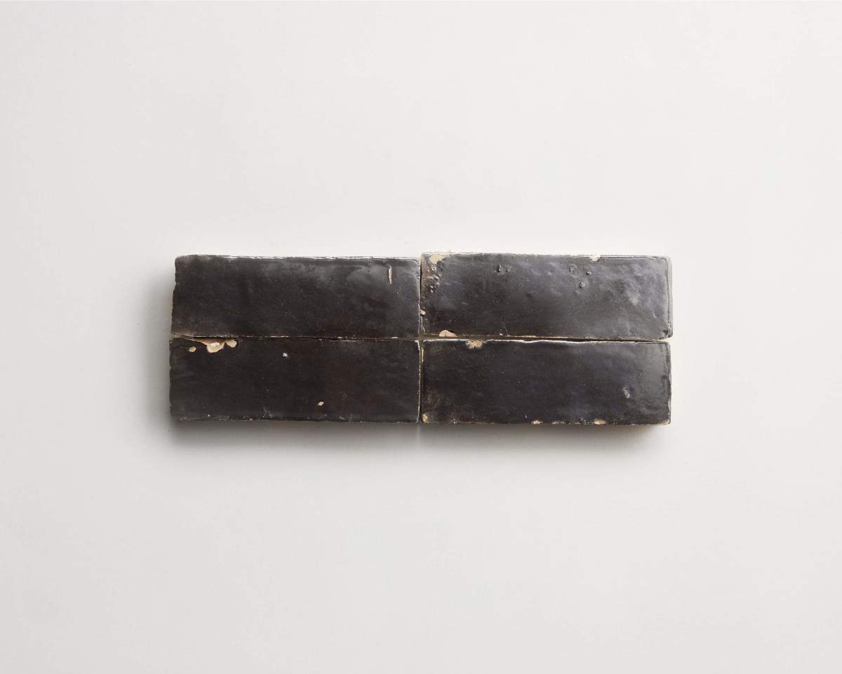 Four rectangular black ceramic tiles with a worn, chipped surface are arranged in a horizontal row on a plain white background.