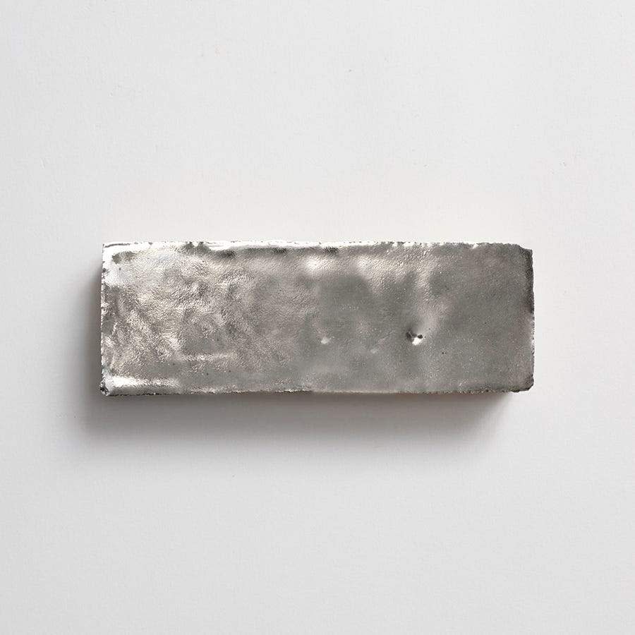 A rectangular silver-colored metal ingot with a rough, uneven surface placed on a plain white background.