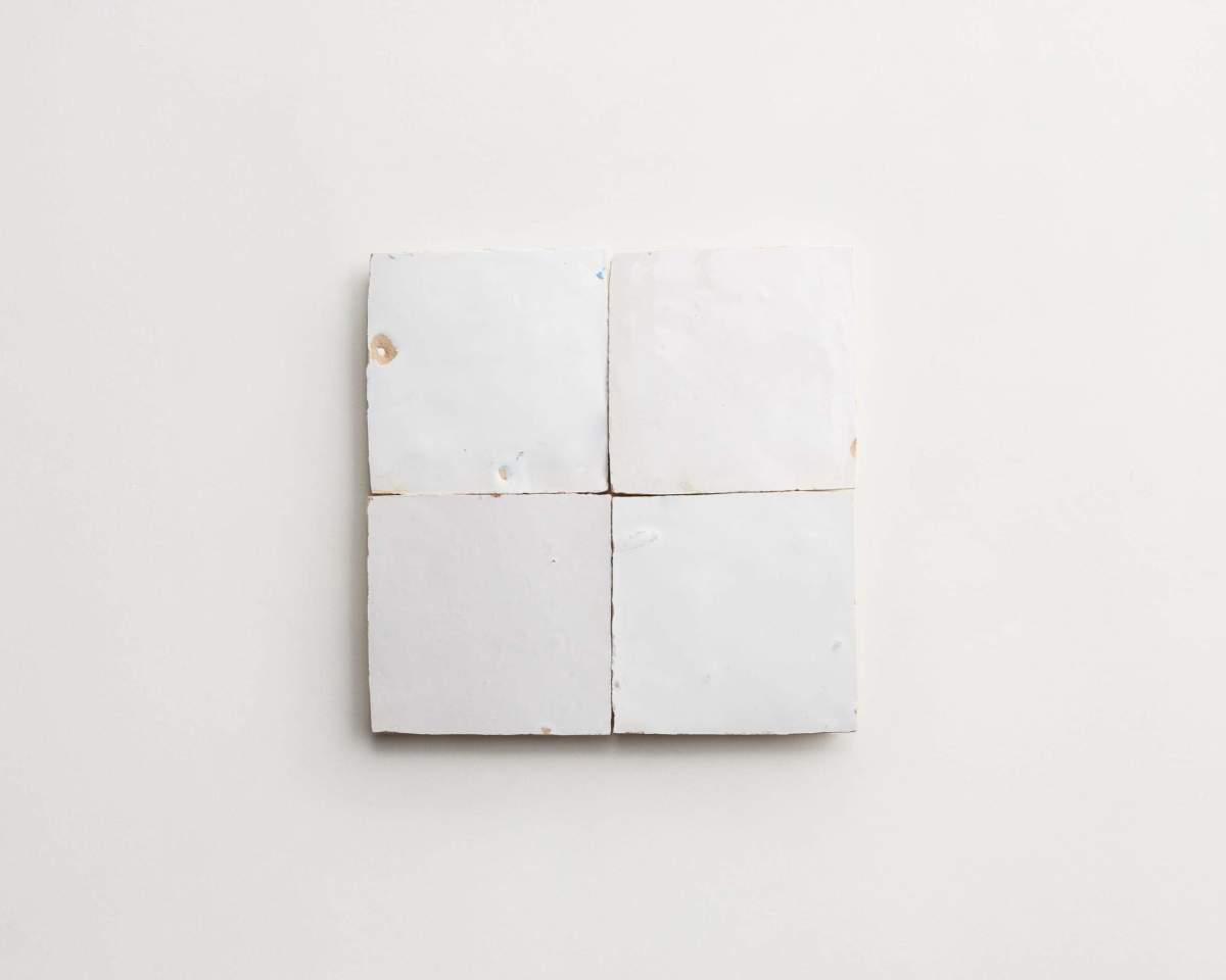 Four white ceramic tiles arranged in a square on a plain, light-colored background.