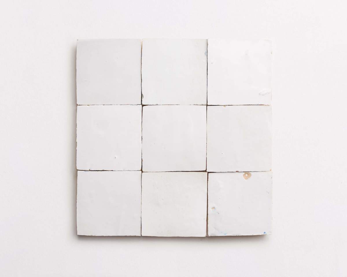 A grid of nine white ceramic tiles arranged in a square on a white background, with slight imperfections and a small brown spot on one tile.