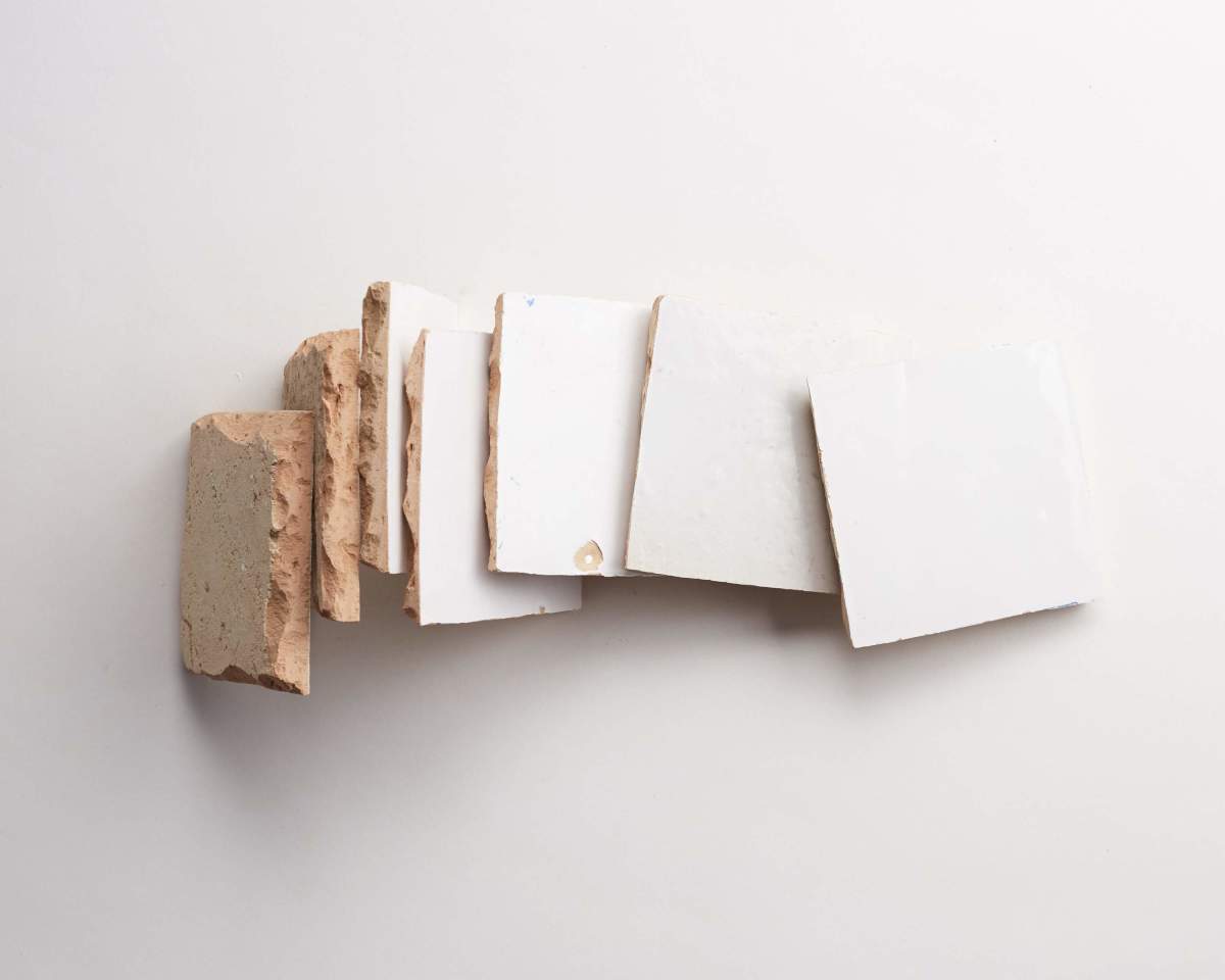 Six square ceramic tiles are arranged in a row on a white surface, each with a white glazed front and exposed brown clay edges.
