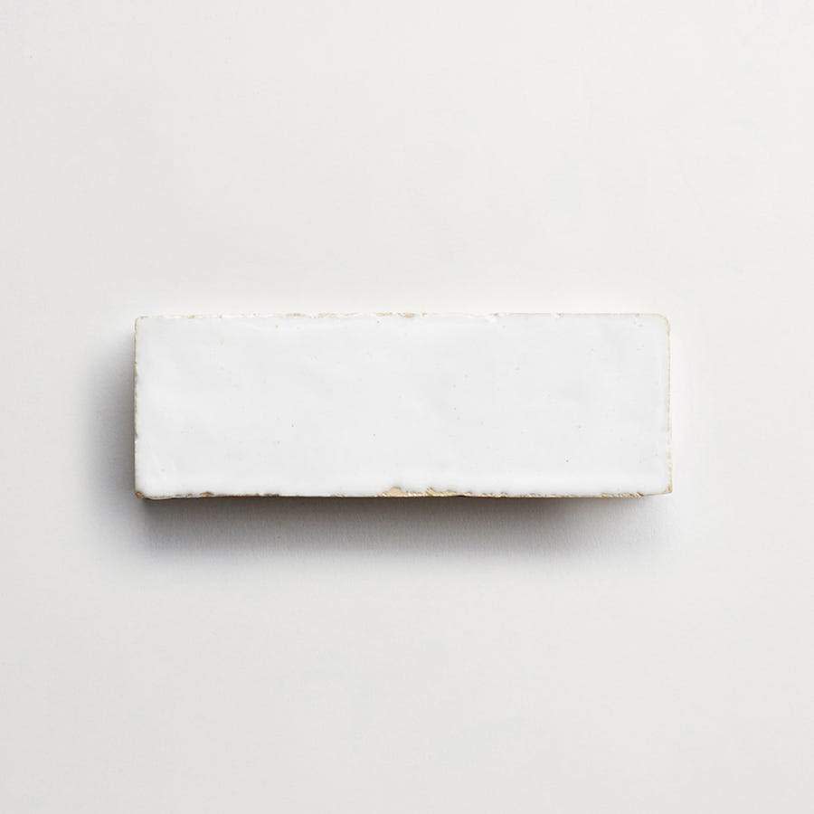 A rectangular white ceramic tile with slightly rough edges placed on a light background.