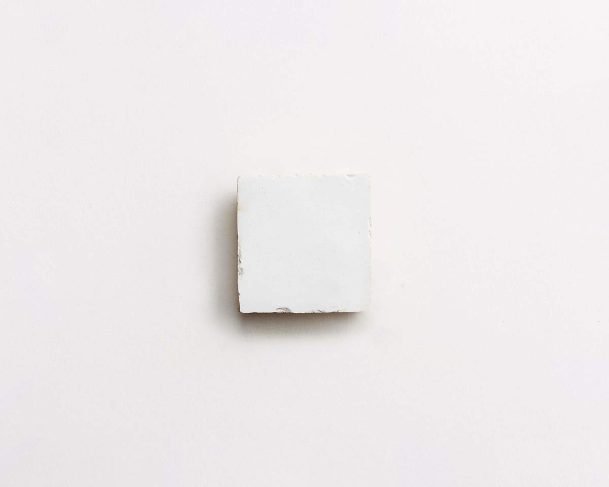 A single white square tile is centered on a plain, light background.