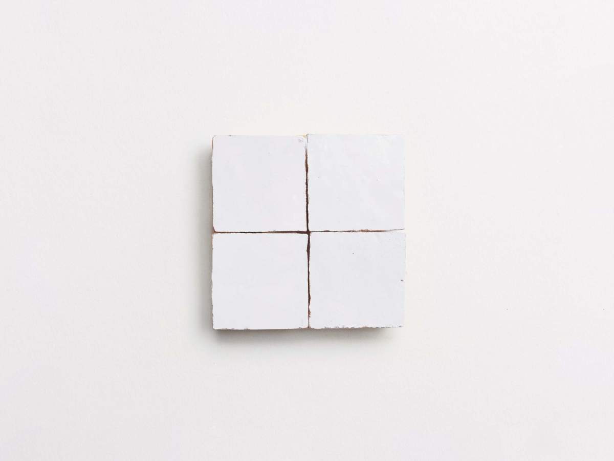Four small, white square tiles are arranged in a 2x2 grid on a plain, light background.