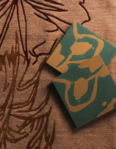 Two green and gold tiles on a textured brown surface with leaf patterns
