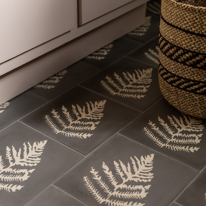 Grey square cement tiles with an off-white colored fern in the center installed on a floor